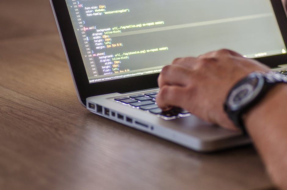 A close-up view of a laptop screen displaying lines of code on a dark background, positioned on a wooden desk in a workspace. Next to the laptop, there is a ceramic coffee mug with a beige background 