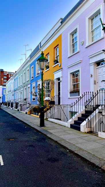 A four-storey red-brick residential building with decorative white trim and black wrought iron balconies on the upper floors, situated on a street with a clear blue sky overhead. The ground floor feat